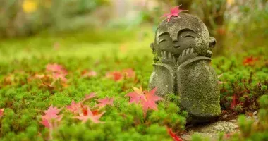 Red Maple leaf on head of little Japanese Buddhist monk doll rock in Japanese Garden